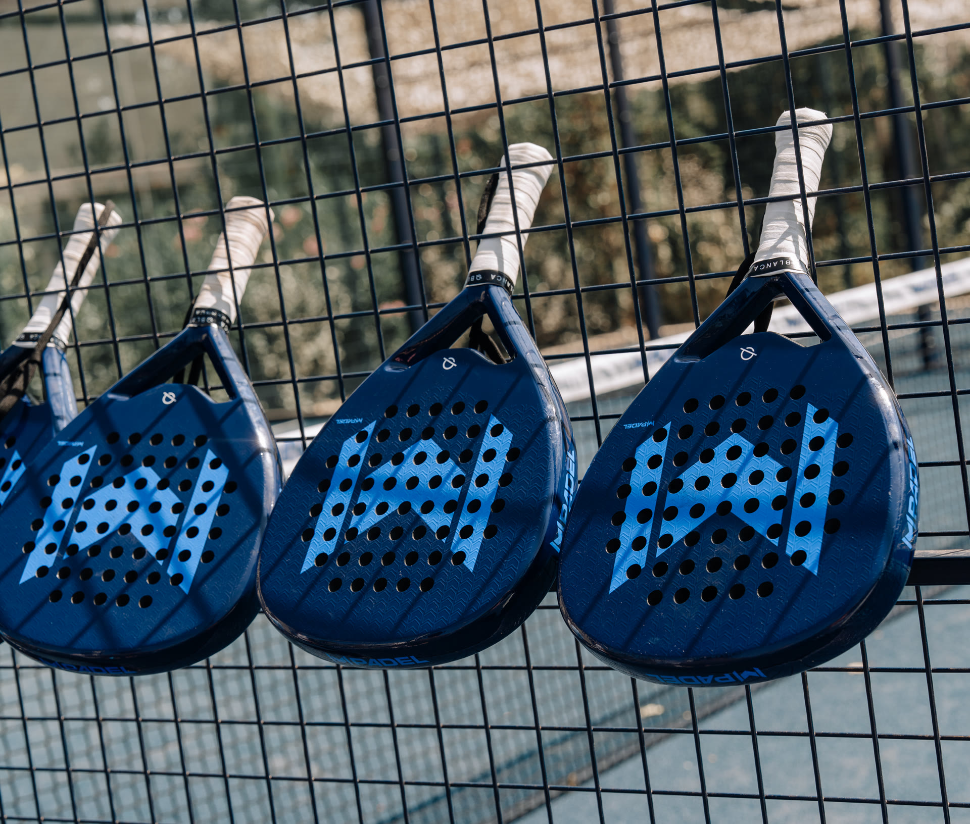Raquettes de padel Mouratoglou accrochées au grillage d’un court